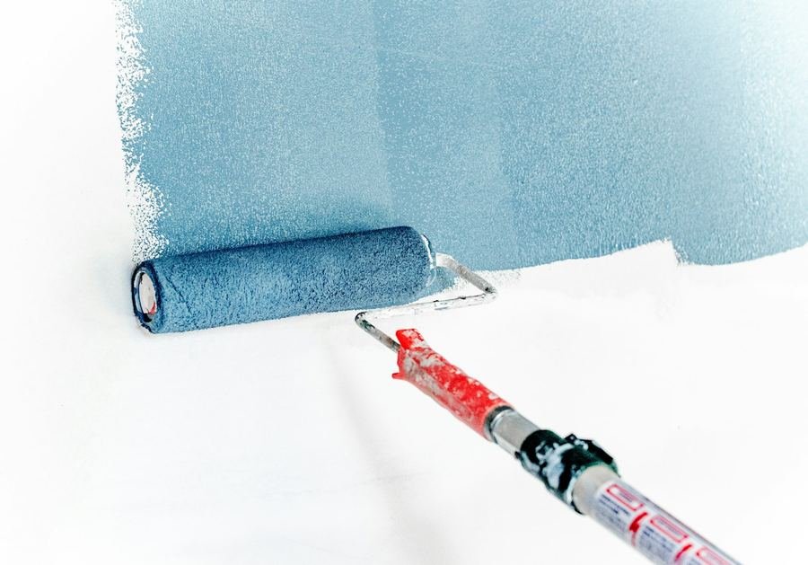 Paint roller applying fresh blue paint to a wall